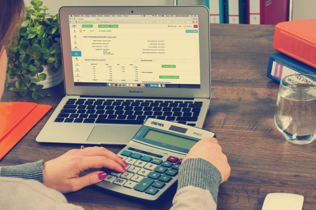 Unseen woman with red nails works on taxes with a laptop and calculator