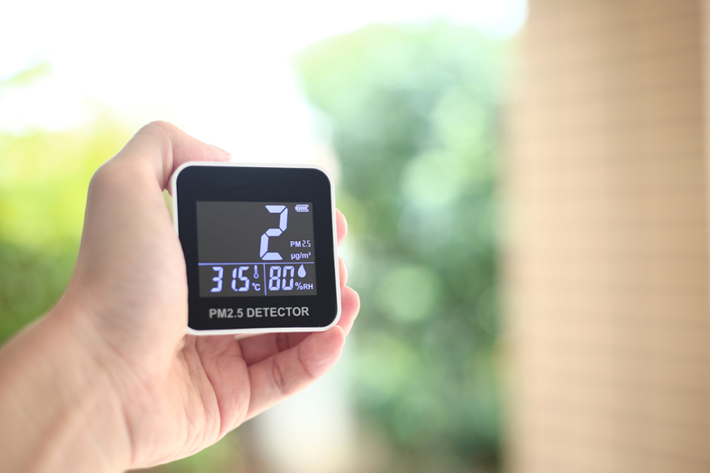 A human hand holds a device measuring dust particles and other data for clean air