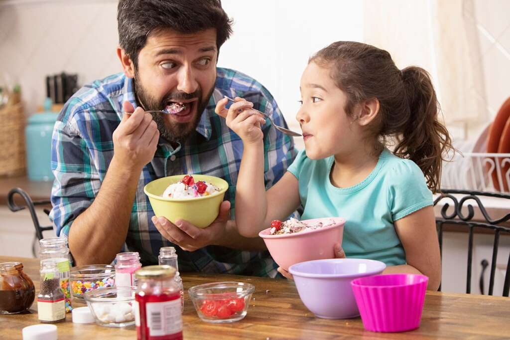 Dad and daughter laugh together over ice cream sundaes, enjoying Summer vacation comfortably at home - the way it should be. Find out how All American Heating can help you make sure your home cooling system is the most energy-efficient it can be.