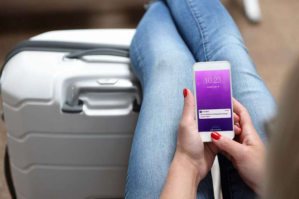 A traveling woman checks her smart phone as she receives an alert about the temperature in her home from her ecobee Smart Thermostat