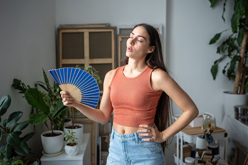 A fit and attractive woman fans herself manually as she is very sweaty.